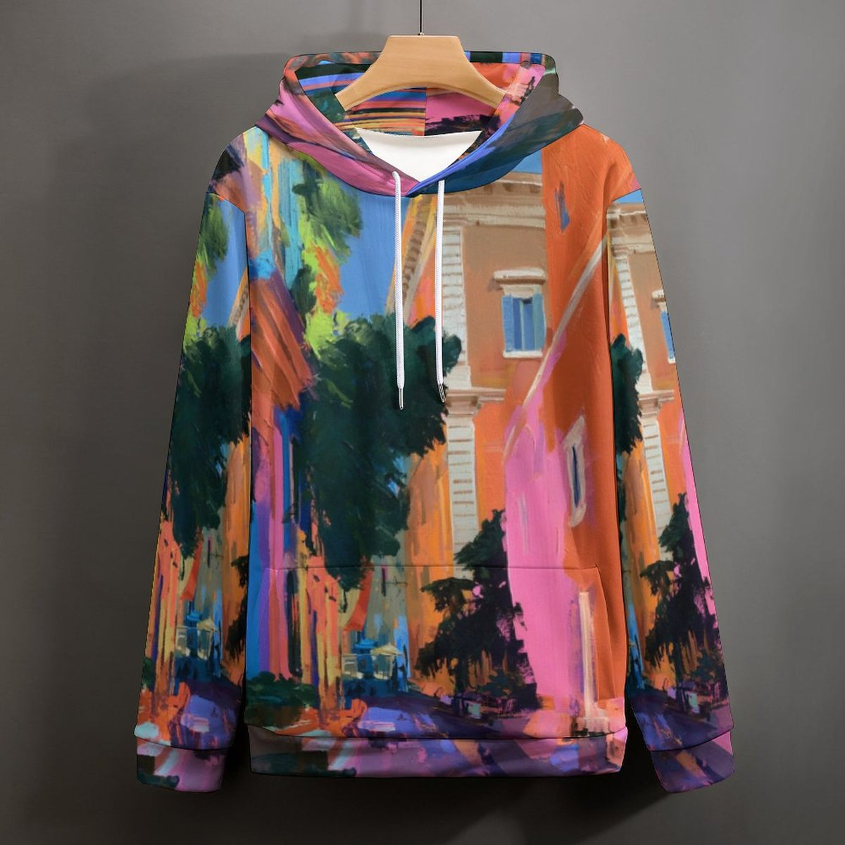 A multicolor pullover hoodie featuring an artistic, painterly print of a street scene with orange buildings, green trees, and blue sky, hanging on a wooden hanger against a dark gray background.