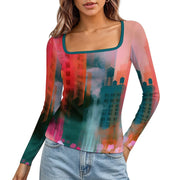 A woman wearing a long-sleeve scoop-neck top with an abstract cityscape print in pink, teal, orange, and red tones, paired with light blue jeans against a plain white background.