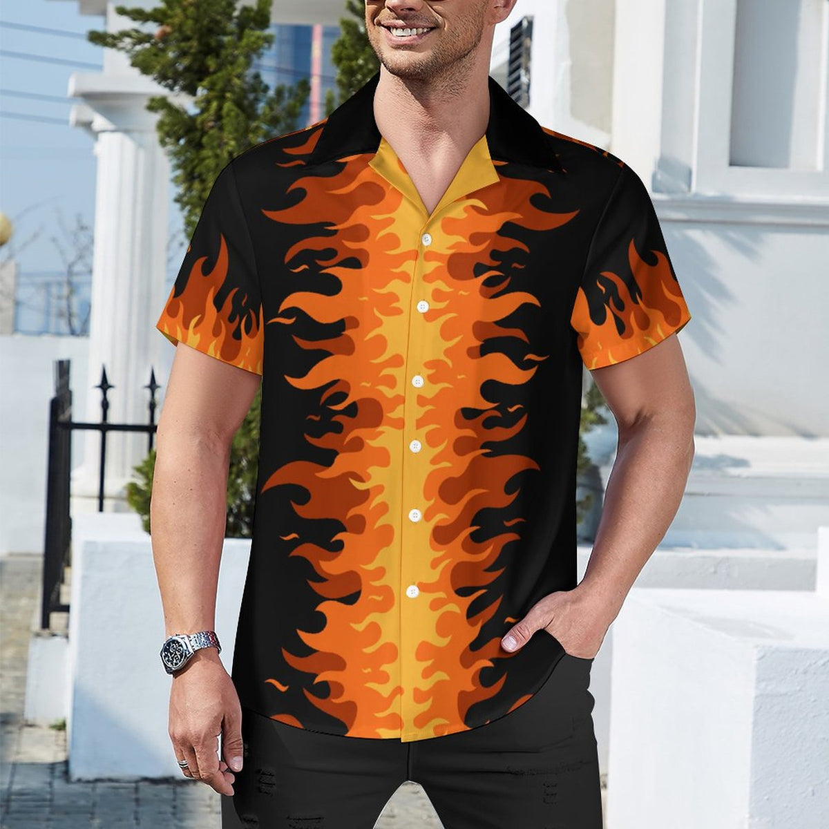 A man wearing a short-sleeve button-up camp shirt with a bold orange and black flame pattern, standing outdoors in front of a white building.