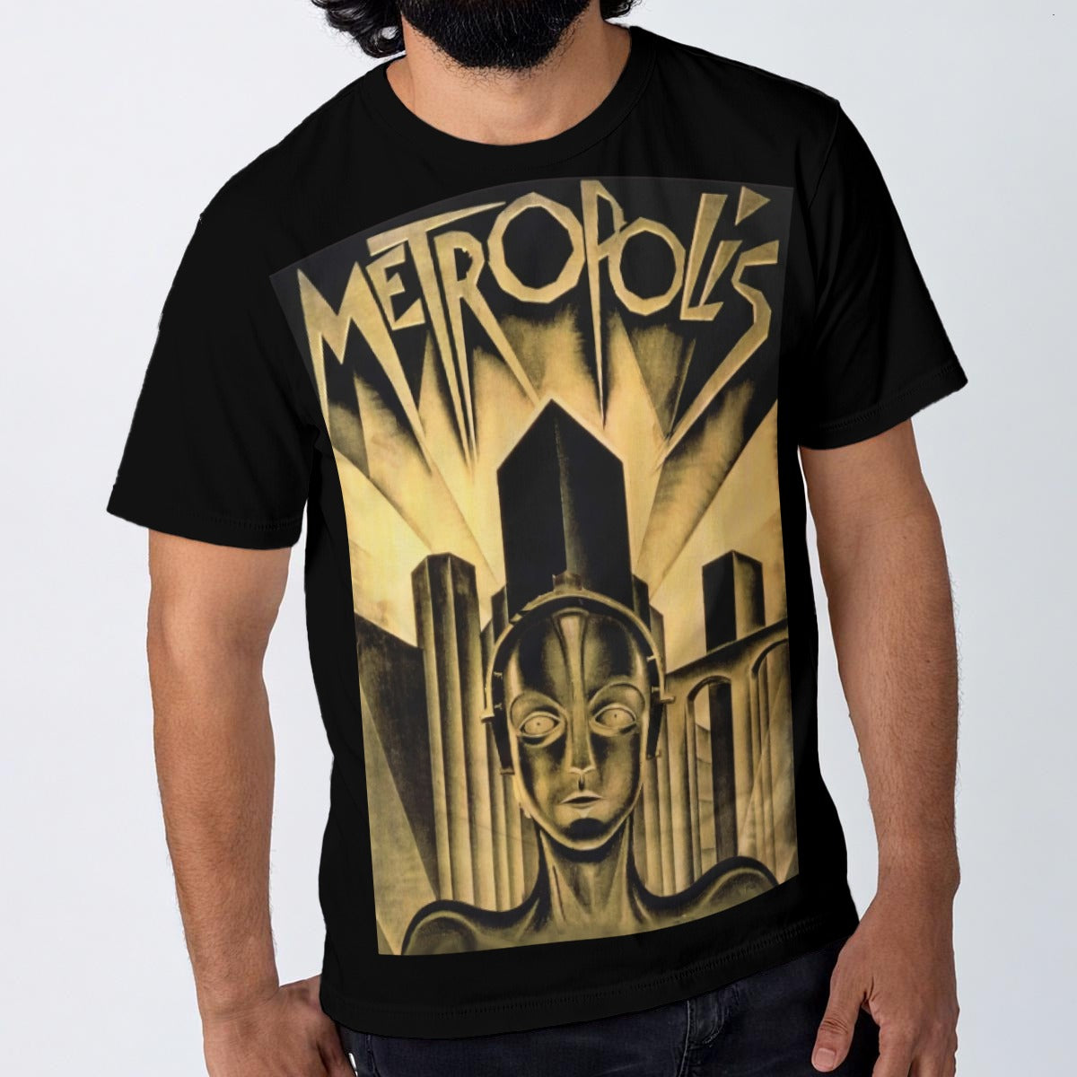 A man wearing a black short-sleeve t-shirt with a large vintage-style Art Deco graphic on the front. The graphic features the word 'METROPOLIS' in stylized gold lettering above a geometric cityscape and face design in gold and beige tones, set against a plain light gray background.