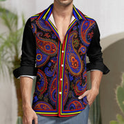 A man wearing a long-sleeve button-up shirt with a black base and a vibrant multicolor paisley print in red, blue, orange, and yellow, styled with light blue jeans.