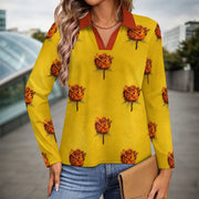 A woman wearing a long-sleeve yellow collared shirt with an all-over orange rose print, paired with blue jeans and holding a tan clutch in an outdoor urban setting.