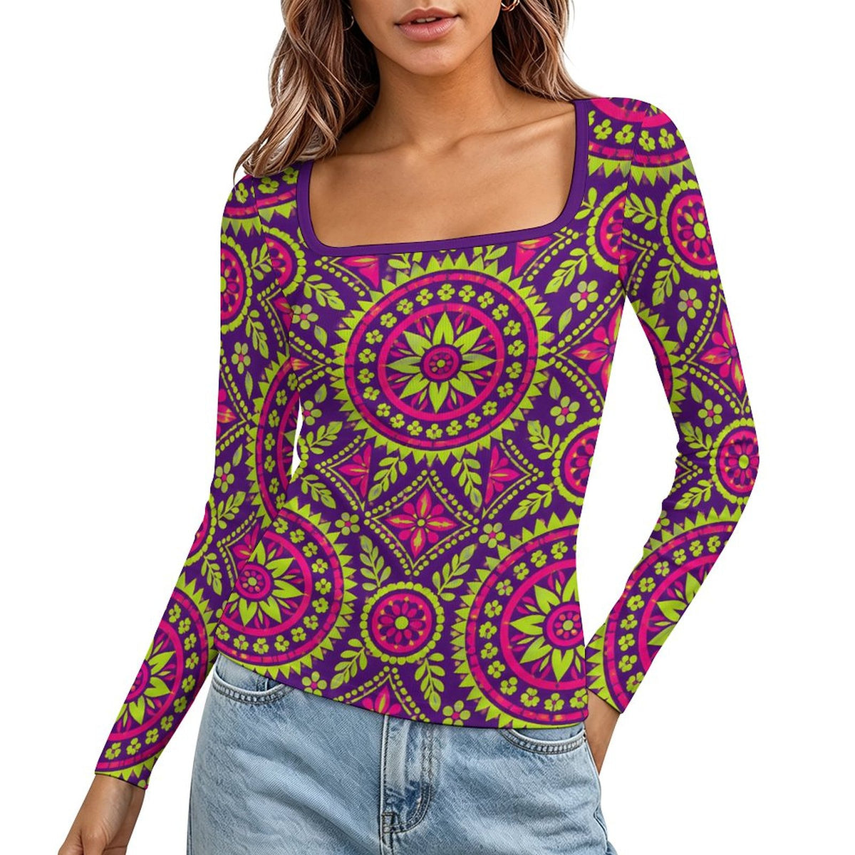 A woman wearing a long-sleeve scoop-neck top with a vibrant magenta and lime green mandala pattern on a purple base, paired with light blue jeans against a plain white background.