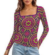 A woman wearing a long-sleeve scoop-neck top with a vibrant magenta and lime green mandala pattern on a purple base, paired with light blue jeans against a plain white background.