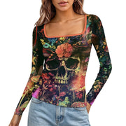 A woman wearing a long-sleeve scoop-neck top with a vibrant, multicolored sugar skull and floral print, paired with light-wash blue jeans against a plain white background.
