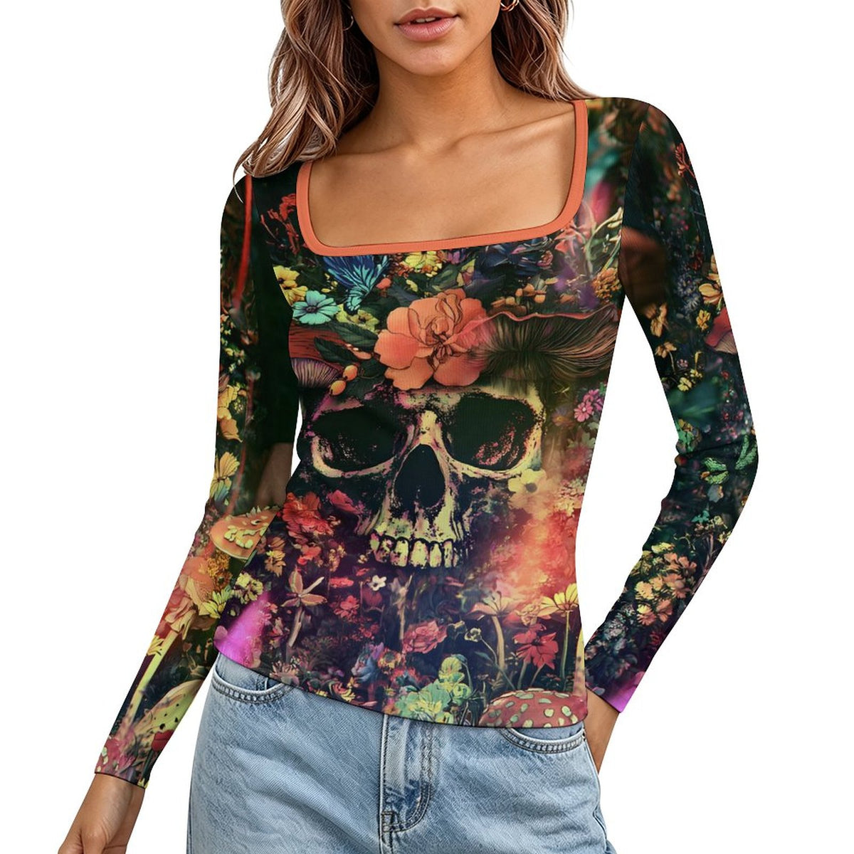 A woman wearing a long-sleeve scoop-neck top with a vibrant, multicolored sugar skull and floral print, paired with light-wash blue jeans against a plain white background.