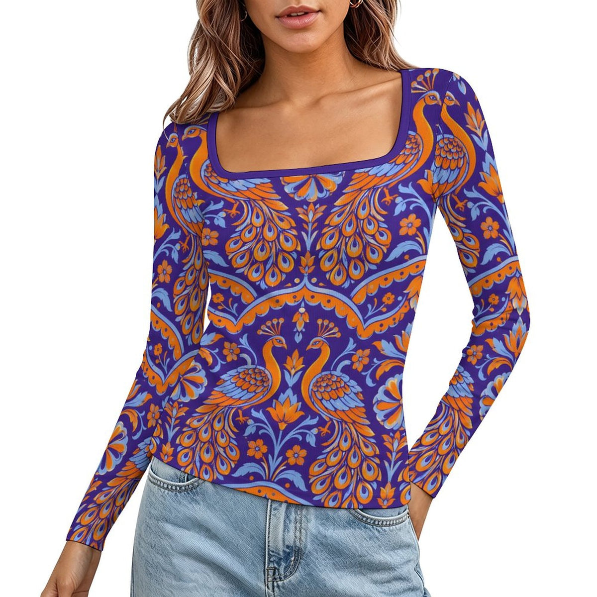 A woman wearing a long-sleeve scoop-neck top with a vibrant purple, orange, and blue peacock pattern, paired with light-wash blue jeans against a plain white background.